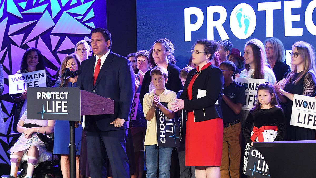 Fl Gov. Ron DeSantis speaks at a podium with pro-life supporters behind him at a Florida church