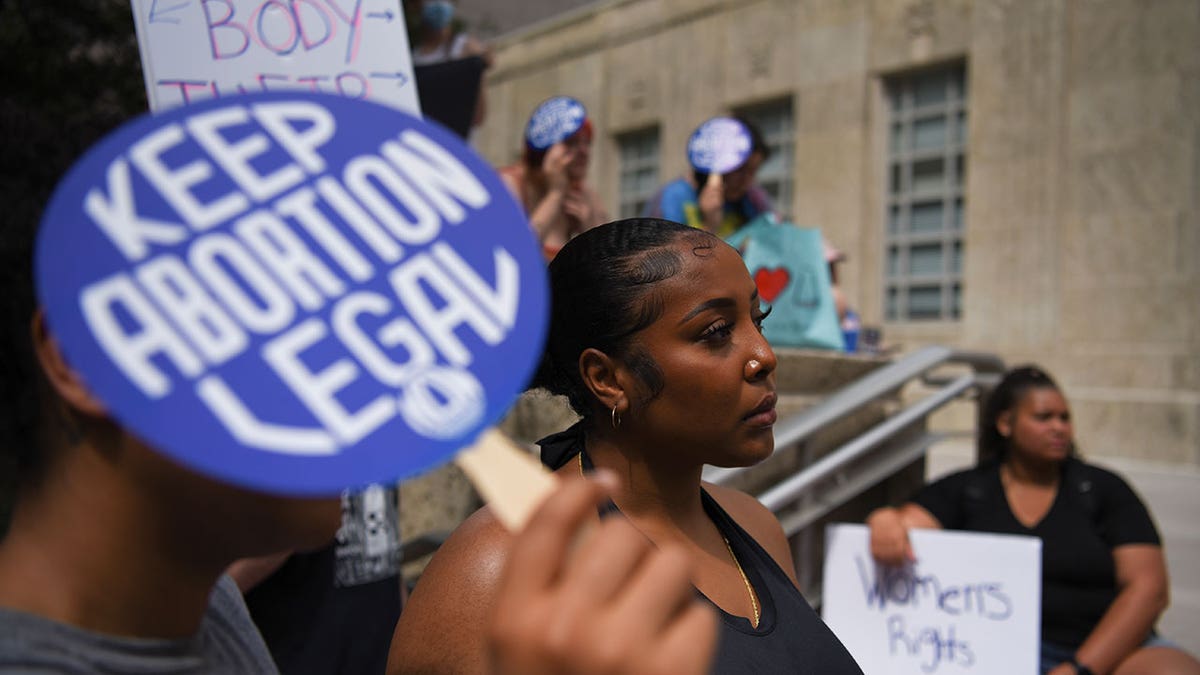 Pro-choice advocates stand outside with signs, one sign saying "Keep Abortion Legal"