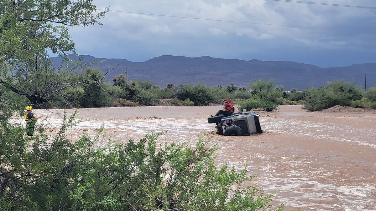 floodwaters swirl around overturned vechile