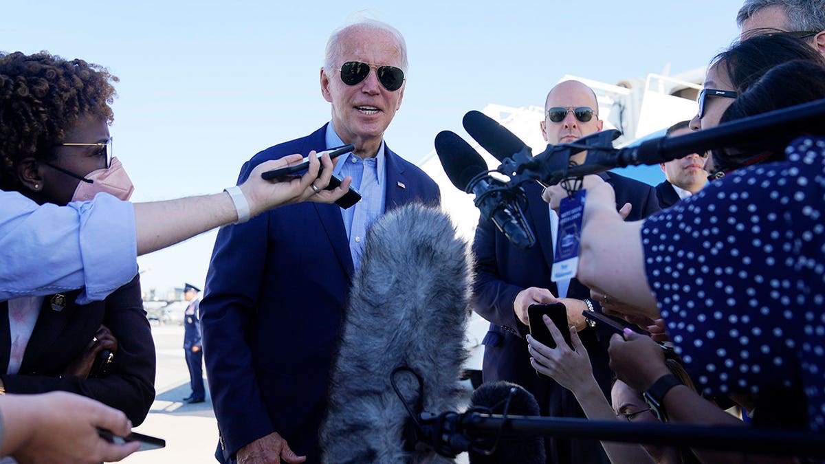 President Joe Biden stands outside in daytime, surrounded by reporters and press people