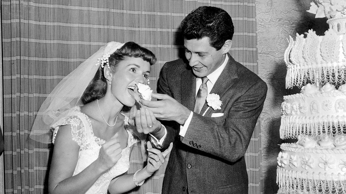 Eddie Singer and Debbie Reynolds eating cake during their wedding in a black and white photo