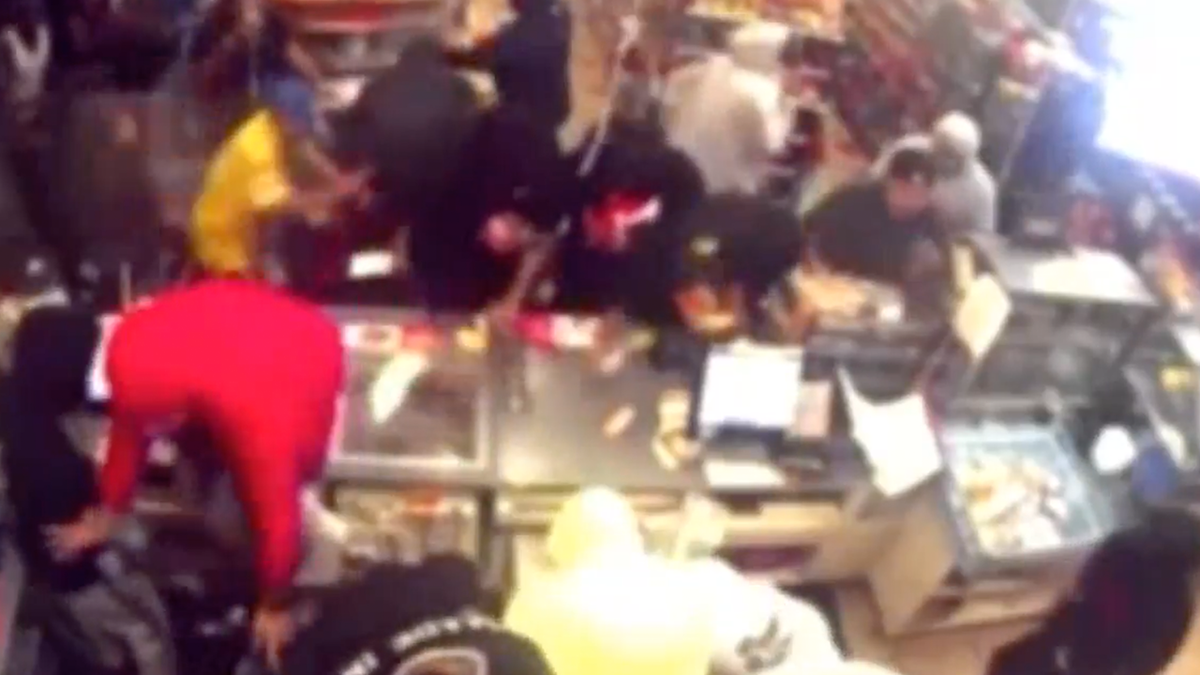 Still from a video shows a mob of people inside a Los Angeles 7-Eleven stealing goods and knocking over a protective shield around a counter