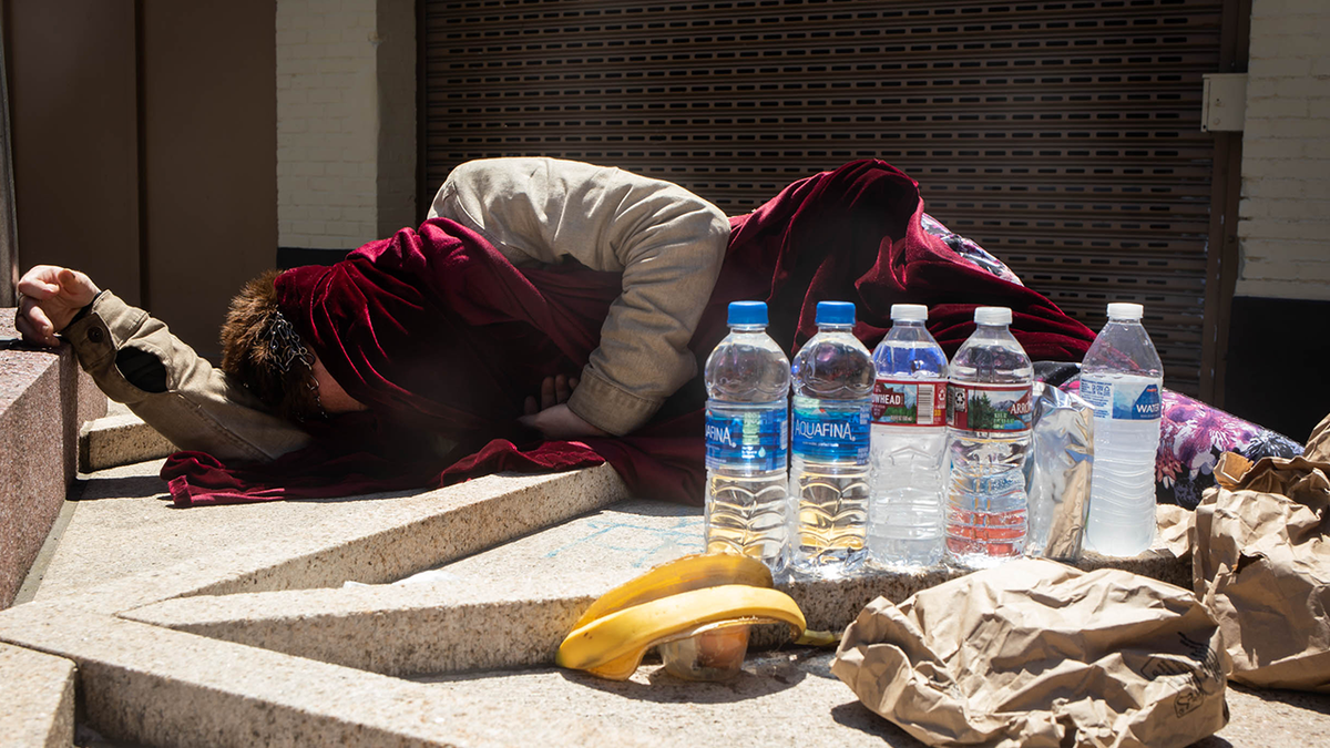 Photo shows homeless person sleeping on street during heatwave with face covered 