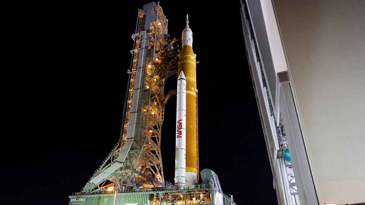 NASA's orange and white Artemis rocket on launch pad with dark skies overheard 