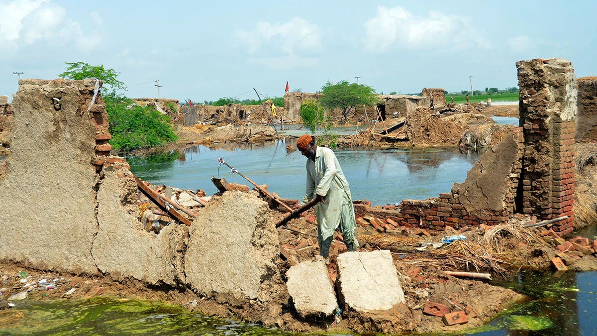 A Pakistani man walks along a destroyed path with a body of water behind him 