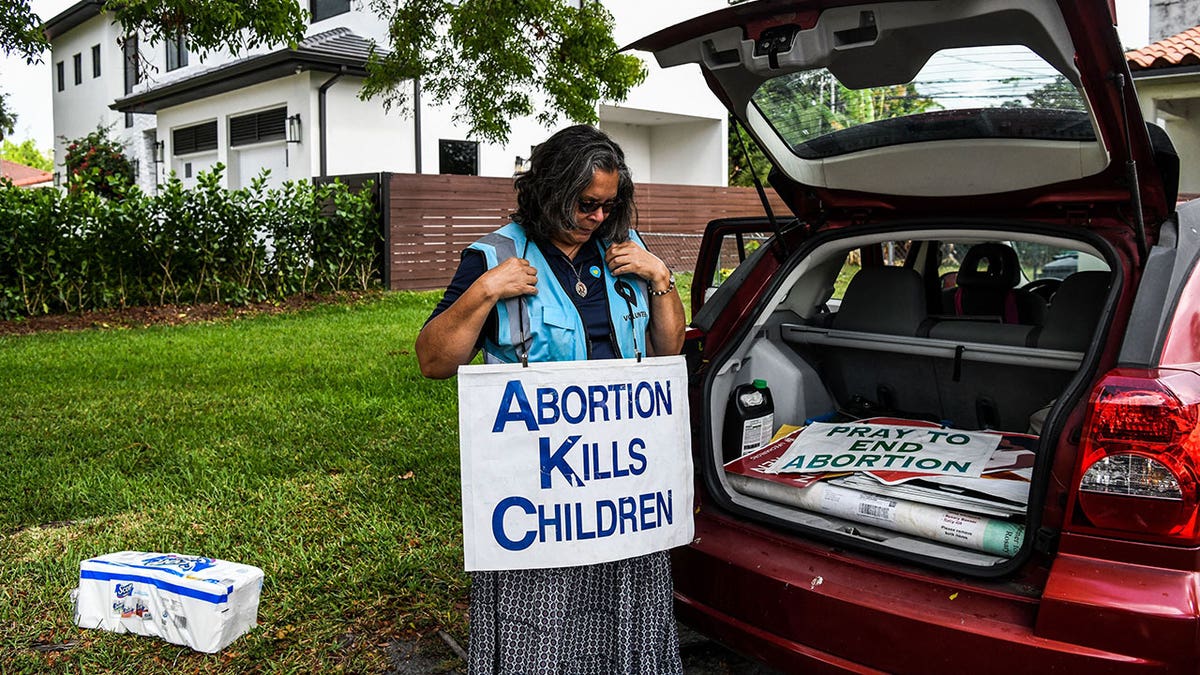 Anti-abortion activist where's a sign that says "Abortion kills children" as she stands behind her car