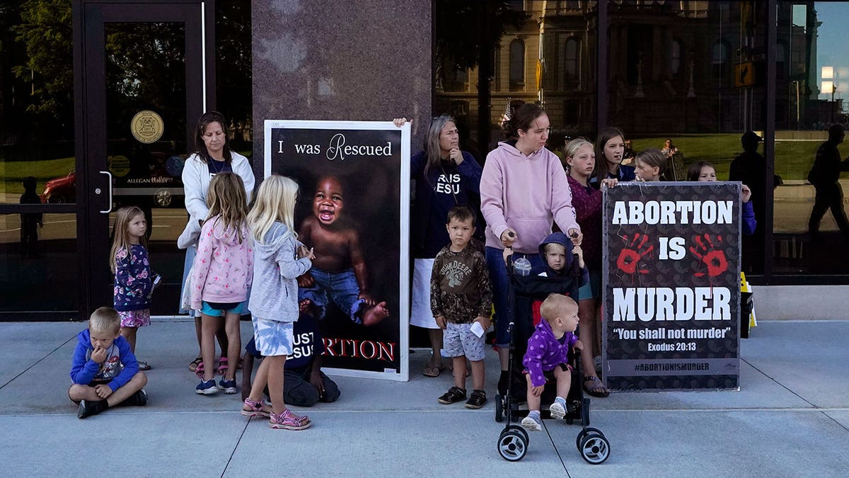 Pro-life advocates stand outside of a building with signs saying "Abortion is murder"