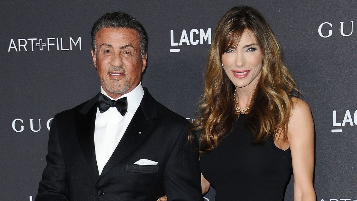 Actor Sylvester Stallone wears a black tux on red carpet with his wife Jennifer Flavin wearing a black dress