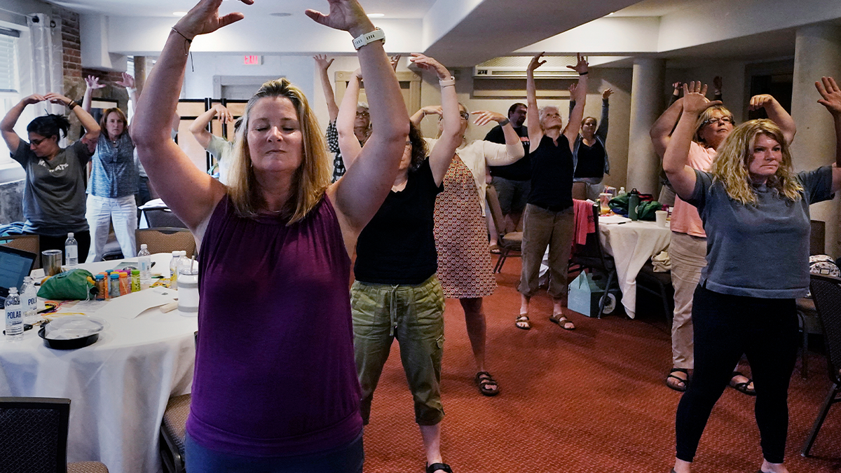 Photo shows teachers taking part in exercise to help alleviate stress and burnout, with their hands stretched above their heads.