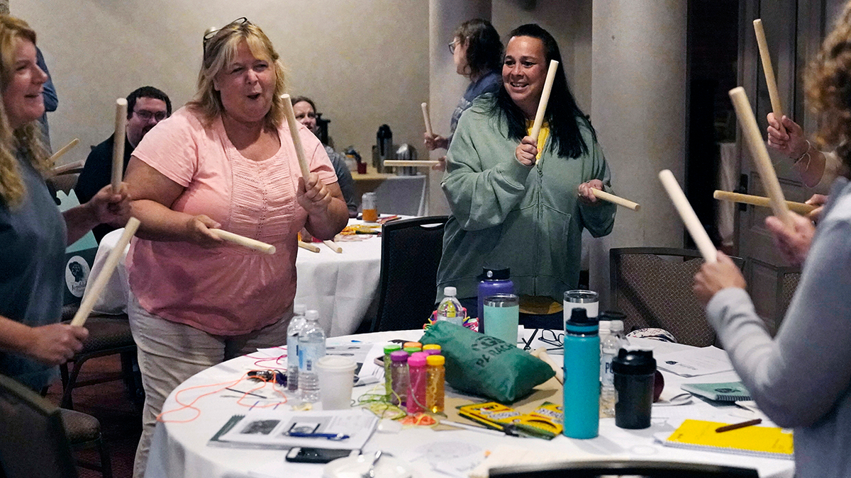 Photo shows teachers tapping wooden sticks during exercise to prevent burnout and increase mental health.