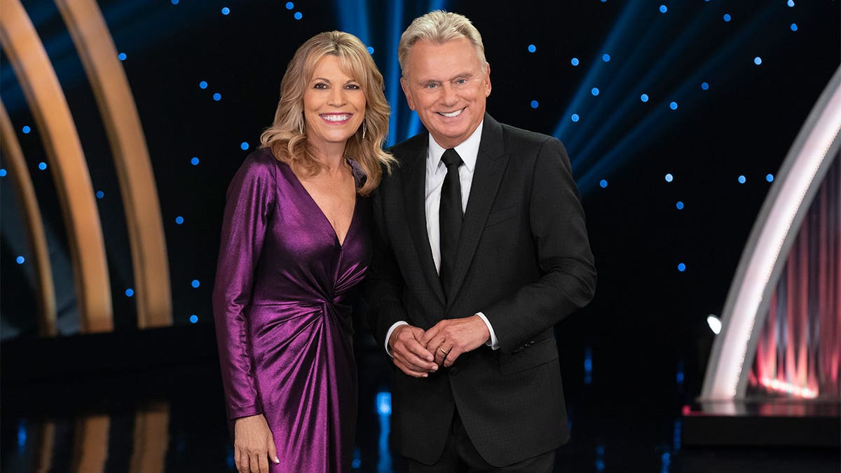 Vanna White in a purple dress and Pat Sajak in a black suit and tie