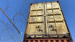 Razor wire lays along shipping containers at border
