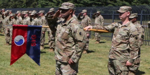 Members of the 29th Infantry Division stand in formation holding a guidon with the division patch.