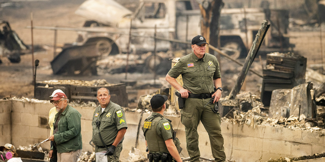 A sheriff's deputy stands at a burned home as search and rescue workers recover the remains of a McKinney Fire victim on Monday, Aug. 1.