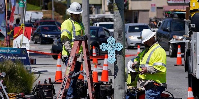 A memorial cross is posted on a traffic pole as technicians replace burned traffic lights and signs after a crash involving multiple cars in the unincorporated Windsor Hills community of Los Angeles on Aug. 5, 2022.
