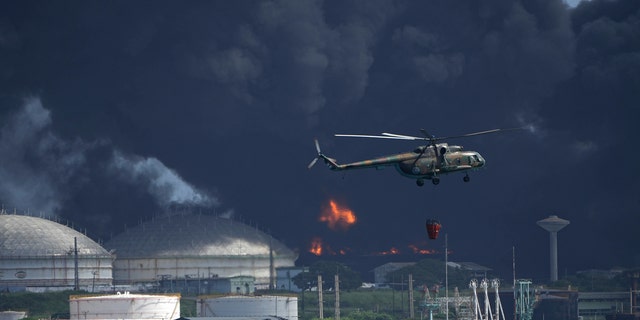A helicopter carrying water flies over the Matanzas Supertanker Base, as firefighters try to quell the blaze which began during a thunderstorm the night before, in Matazanas, Cuba, Saturday, Aug. 6, 2022.