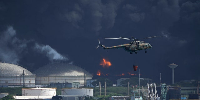 A helicopter carrying water flies over the Matanzas Supertanker Base, as firefighters try to quell the blaze which began during a thunderstorm the night before, in Matazanas, Cuba, Saturday, Aug. 6, 2022.
