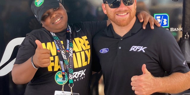 James Bromsey III, left, a sixth-grader at the LeBron James I Promise School in Akron, Ohio, poses with NASCAR driver Chris Buescher in Brooklyn, Michigan. Bromsey was given an all-access trip to Michigan International Speedway on Sunday. Chris Busher's no. 17 Ford had a paint job that highlighted the LeBron James Family Foundation.