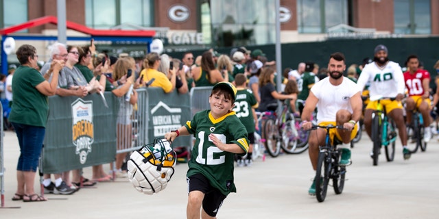 Green Bay Packers tight end Josiah Deguara, third from right, rides a young fan's bike as the fan takes off running with Deguara's helmet during the team's NFL football training camp July 27, 2022, in Green Bay, Wisconsin.