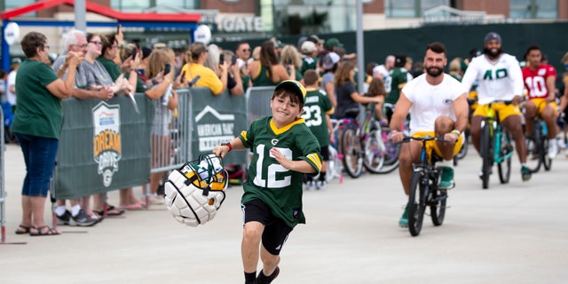 Green Bay Packers tight end Josiah Deguara, third from right, rides a young fan's bike as the fan takes off running with Deguara's helmet during the team's NFL football training camp July 27, 2022, in Green Bay, Wisconsin.