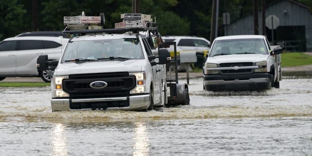 A couple of pickup trucks creep through flood waters in Richland, Miss., following a morning of torrential rains, Wednesday, Aug. 24, 2022.