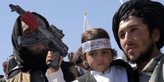 An Afghan boy holds a toy weapon during a celebration marking the first anniversary of the withdrawal of US-led troops from Afghanistan, in front of the U.S. Embassy in Kabul, Afghanistan, Wednesday, Aug. 31, 2022. 
