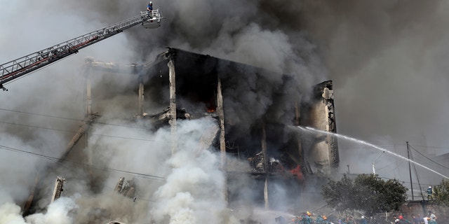 Firefighters extinguish the flames as smoke rises from the Surmalu market about two kilometers (1.2 miles) south of central Yerevan, Armenia on Sunday, August 14, 2022. A massive explosion in a fire storage area fireworks ripped through a market in the capital of Armenia.  At least one person was killed and about 20 others were injured.  Sunday's explosion caused a large fire.  (Vahram Baghdasaryan / Photolure via AP)