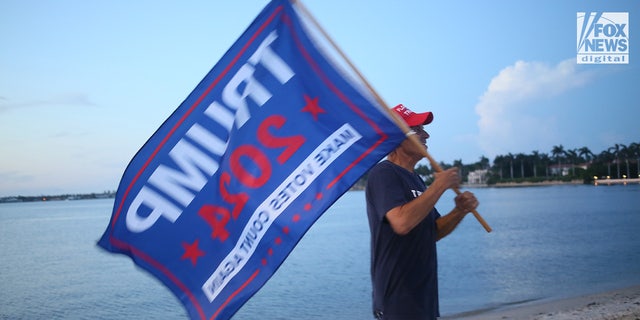 A man with a Trump 2024 flag is pictured outside Mar-a-Lago in Palm Beach, Florida following an FBI raid on Donald Trump's private home.