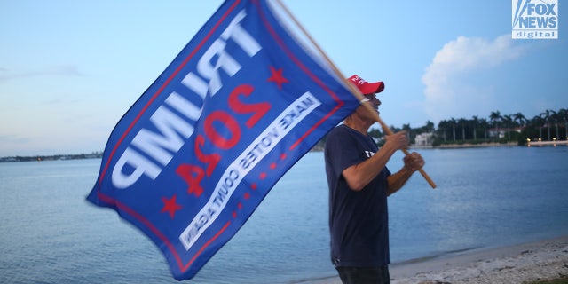 A man with a Trump 2024 flag is pictured outside Mar-a-Lago in Palm Beach, Florida, following an FBI raid on Donald Trump's private home.