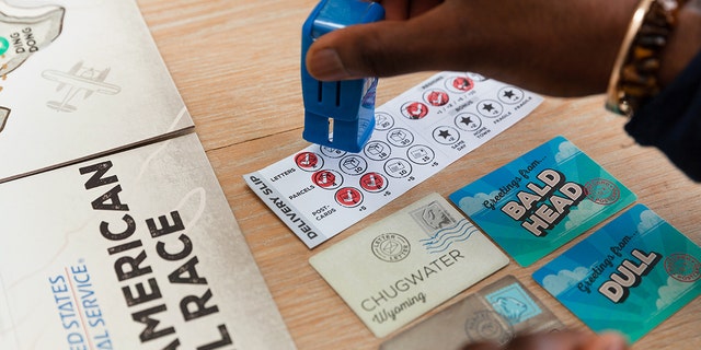 A player stamps a delivery slip with a replica mail collection box stamp while playing the board game USPS: The Great American Mail Race.
