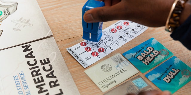A player stamps a delivery slip with a replica mail collection box stamp while playing the board game USPS: The Great American Mail Race.