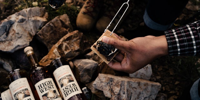 A camper makes a s'more on several bottles of High West Campfire whiskey.