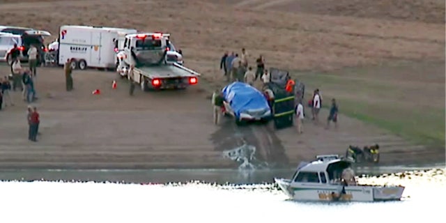 A white SUV is covered by a blue tarp after authorities pulled it from Prosser Creek Reservoir in California late Sunday night.