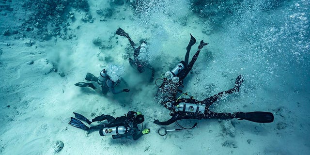Divers are shown searching for buried treasure at the bottom of the sea - the site of a shipwreck in the Bahamas.