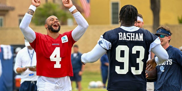 Dallas Cowboys quarterback Dak Prescott (4) celebrates after a play as defensive end Tarell Basham (93) looks on on opening day of NFL football training camp, Saturday, July 30, 2022, in Oxnard, Calif.