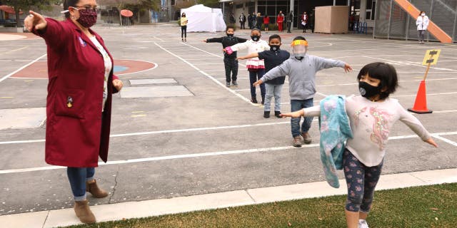 Teacher Lilia Guerrero, left, directs kindergarteners to class as they show 6-feet social distancing on their first day back to class at the 9th Street Elementary School in Los Angeles on April 13, 2021.