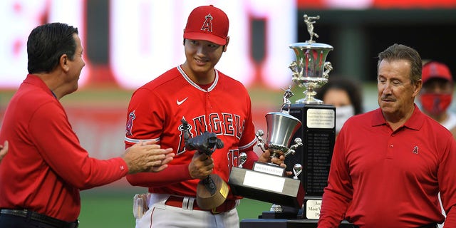 General manager Perry Minasian, left, applauds Shohei Ohtani while Los Angeles Angels owner Arte Moreno waits to give him the Angels Most Valuable Player award before a game against the Seattle Mariners at Angel Stadium of Anaheim Sept. 25, 2021, in Anaheim, Calif. 