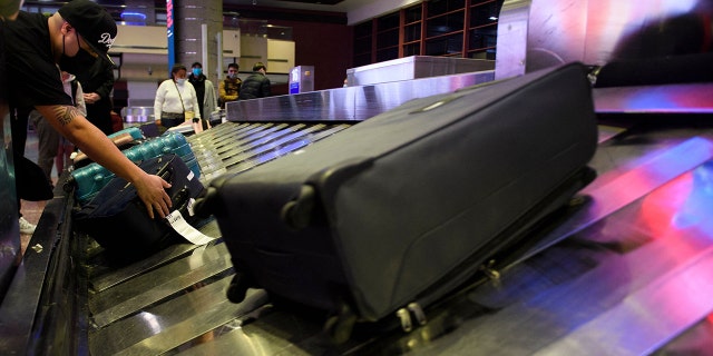 Airline passengers wearing face masks wait to collect bags from a baggage carousel at the Harry Reid International Airport (LAS) on January 2, 2022. 