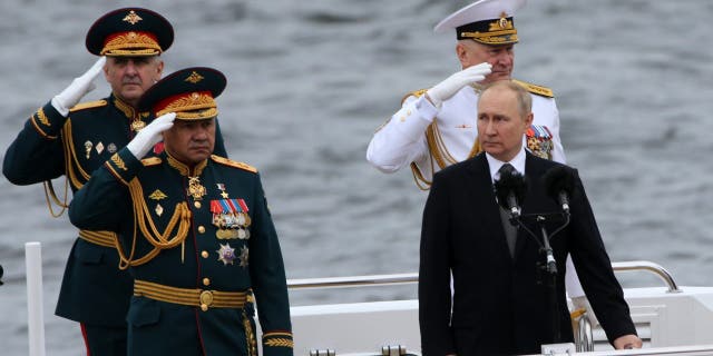 Russian President Vladimir Putin, front right, Defense Minister Sergei Shoigu, left, and Russian Fleet Commander Nikolai Yevmenov, back right, aboard a boat during the Navy Day Parade, July 31 2022, in St. Petersburg, Russia.