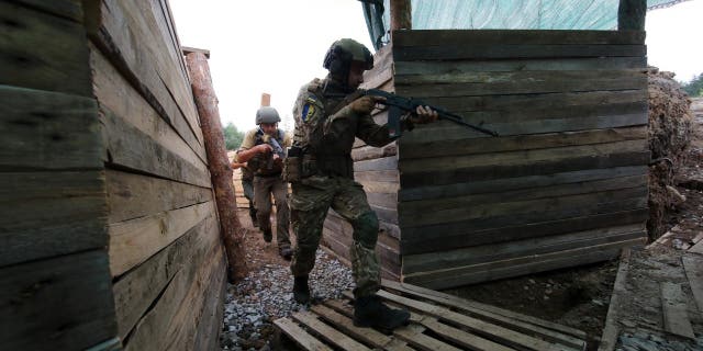 Armed National Guard servicemen walk along a trench at one of the sections of a defence line outside Kharkiv, Kharkiv Region, northeastern Ukraine. 