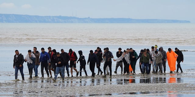 A group of people, believed to be migrants, walk ashore in Dungeness, Kent, following an accident in a small boat in the English Channel on 25 August 2022.