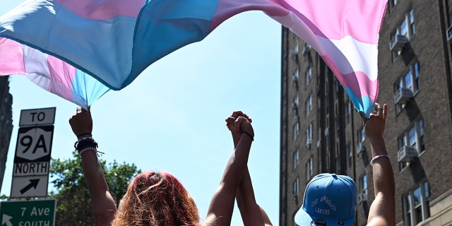 Two trans people hold hands while marching under a trans pride flag in the New York City Pride Parade on June 26, 2022, in New York City.