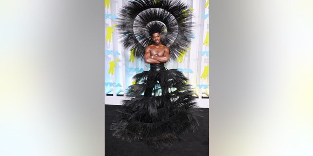 Lil Nas X went shirtless as he walked the VMAs red carpet wearing a sheer black skirt to match an oversized hat.