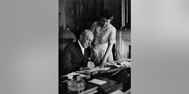 Woodrow Wilson (1856-1924), president from 1913-1921, goes over papers as his second wife, Edith Bolling Galt Wilson (1872-1961) looks on.