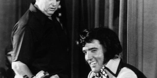 Elvis Presley is seen holding court at a press conference to publicize his show at Madison Square Garden later that night while Colonel Tom Parker looks on at the Hilton Hotel on June 9, 1972, in New York City.
