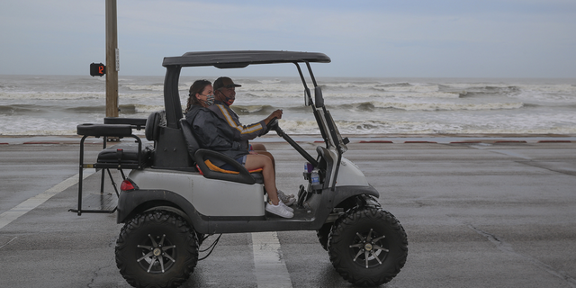 People ride a golf cart on Seawall Boulevard as waves from Hurricane Laura roll in on Aug. 26, 2020 in Galveston, Texas