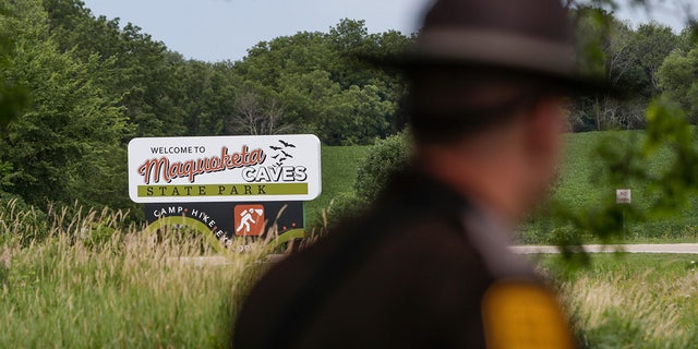 An Iowa State Patrolman walks past a Maquoketa Caves State Park sign as police investigate a shooting that left several people dead, Friday, July 22, 2022, in Maquoketa, Iowa. The campground was evacuated in the wake of the shooting. 