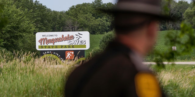 An Iowa State Patrolman walks past a Maquoketa Caves State Park sign as police investigate a shooting that left several people dead, Friday, July 22, 2022, in Maquoketa, Iowa. The campground was evacuated in the wake of the shooting. 