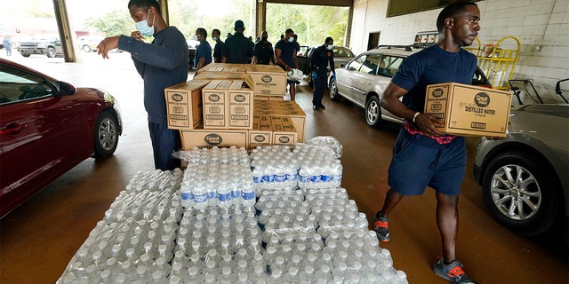 Firefighters and recruits for the Jackson, Miss., Fire Department carry cases of bottled water to residents vehicles, Aug. 18, 2022, as part of the city's response to longstanding water system problems.