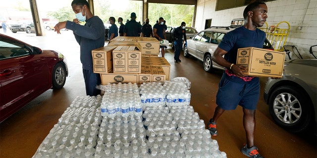 Firefighters and recruits for the Jackson, Mississippi, Fire Department carry cases of bottled water to residents vehicles, Aug. 18, 2022, as part of the city's response to longstanding water system problems.